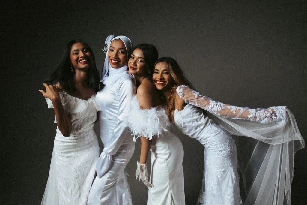 Four women posing in white dresses against The Mighty Grey's dark backdrop.